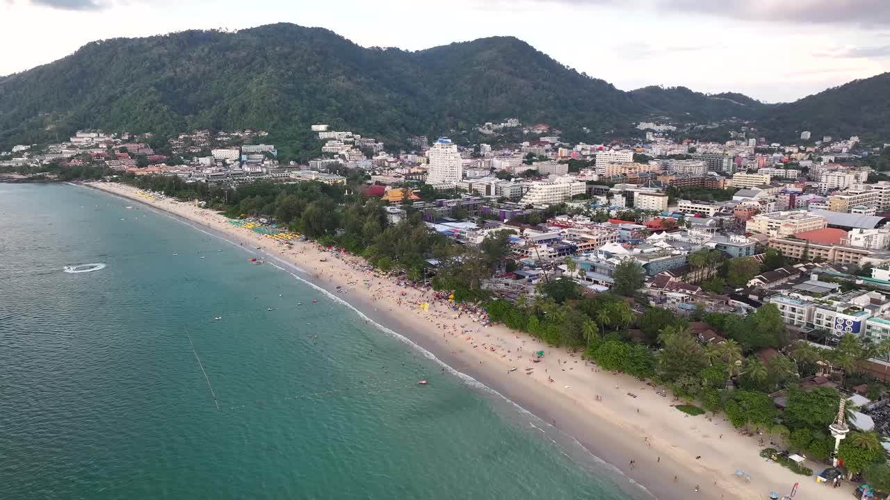 Long Stretch Of Patong Beach With Forested Hills View. Beachfront Hotels On Shore In Phuket, Thailand. aerial pullback shot