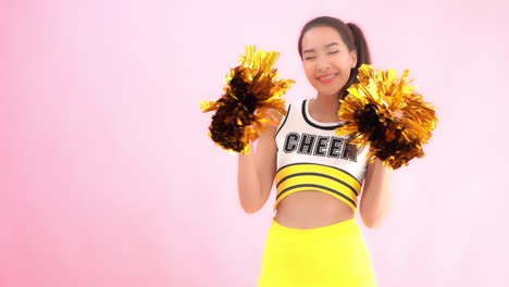 a cute cheerleader in a uniform smiles while she shakes her sparkly pom-poms