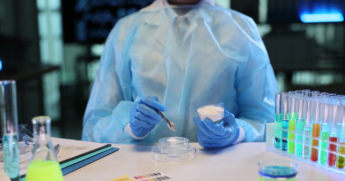 Chemist wearing full protective clothing examines white powder