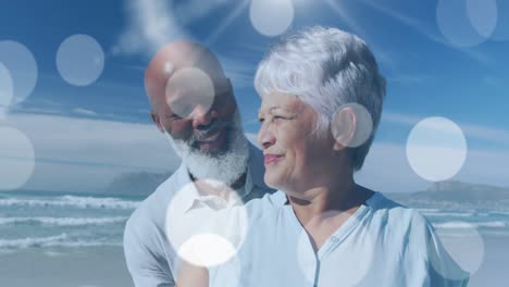 Animation-of-happy-senior-african-american-couple-embracing-at-beach-over-light-spots