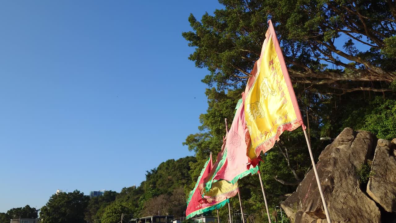 Static shot of multicolor flags of a Chinese Temple waving on a windy day in Lei Yu Mun, Hong Kong