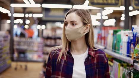 Mujer-Con-Máscara-Protectora-Caminando-Por-El-Supermercado-Entre-Pasillos,-Buscando-Algo