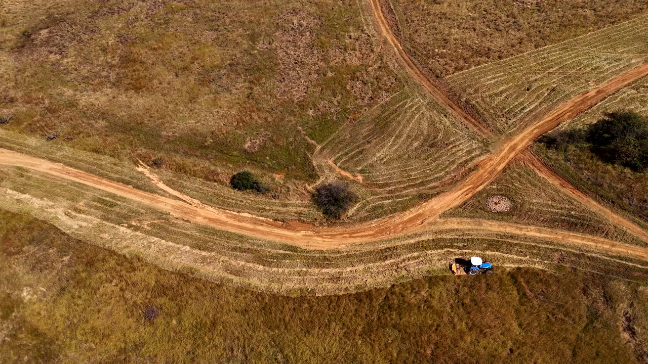Farm management as tractor with mower cuts overgrown grassy edge of road, aerial