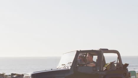 Happy-caucasian-gay-male-couple-in-car-admiring-the-view-and-pointing-on-sunny-day-at-the-beach