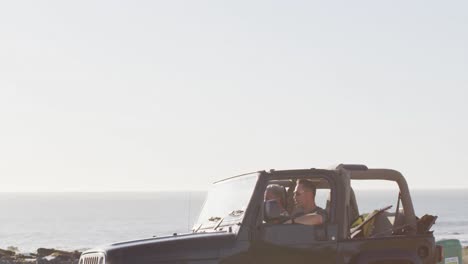 feliz pareja masculina gay caucásica en el coche admirando la vista y señalando el día soleado en la playa