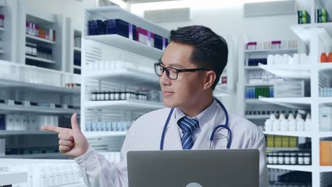 アジア人の男性医師がステトスコープを持ってラップトップを握り横を指し薬局で笑顔で