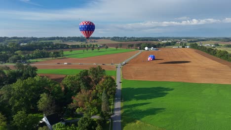 cinematic drone flight over rural road surrounded by agricultural fields and flying hot-air balloon in background - backwards drone shot