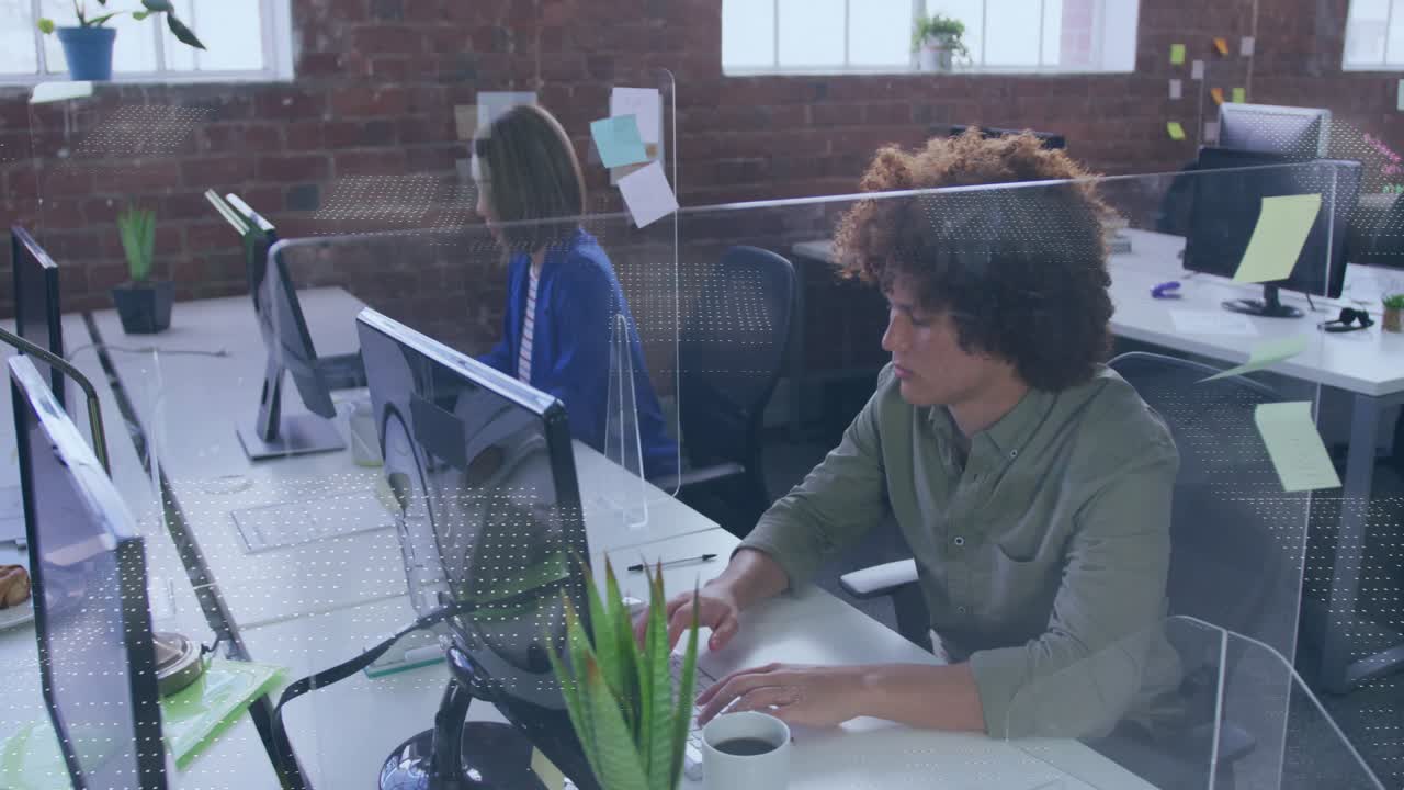 Two colleagues typing at desk data feed initiating overlay over monitors showing tech data