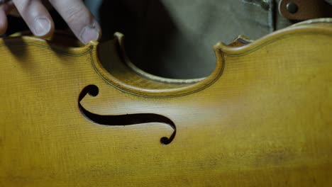 close-up of a violin maker antiquing the ribs and edges of the center bout of his violin, simulating natural wear with dark pigments and tool marks, creates authentic aged character in the instrument