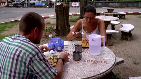 thai street food. man and woman eating noodles with vegetables