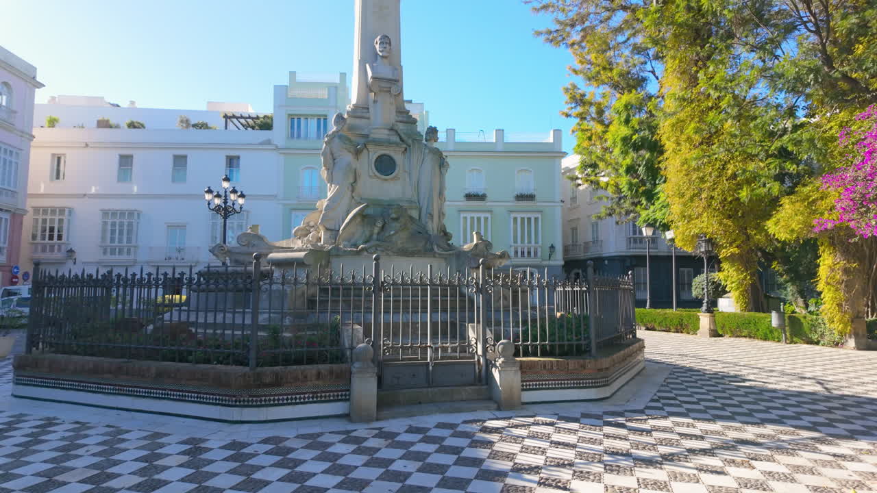 Monumental statue in a plaza with green trees Monument to the Marquis de Comillas in C&aacute;diz, Spain