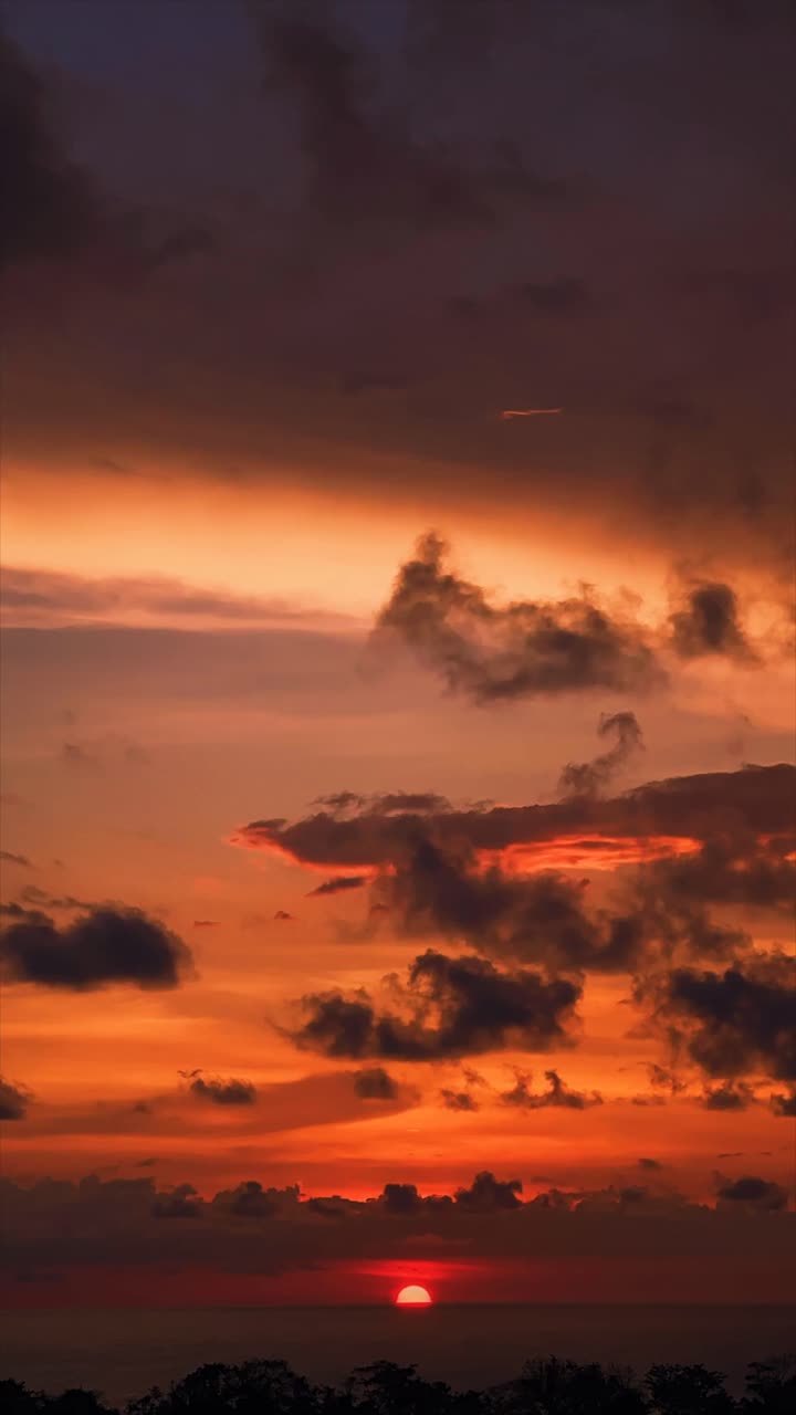 Vertical video of sun going down over the ocean horizon with clouds passing by