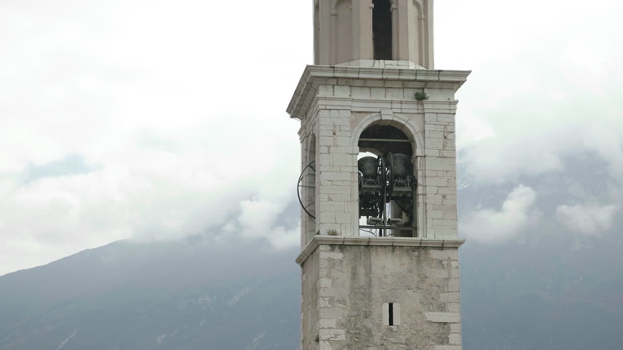 Close-up handheld shot of bells tolling in a church tower with misty mountains in background
