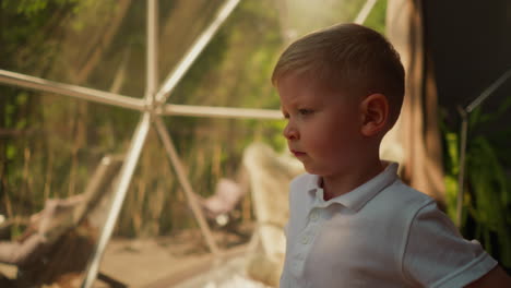 child stretches back in glamping hotel. tired little boy spends time in deluxe camping dome cabin. calm kid rests at eco resort closeup