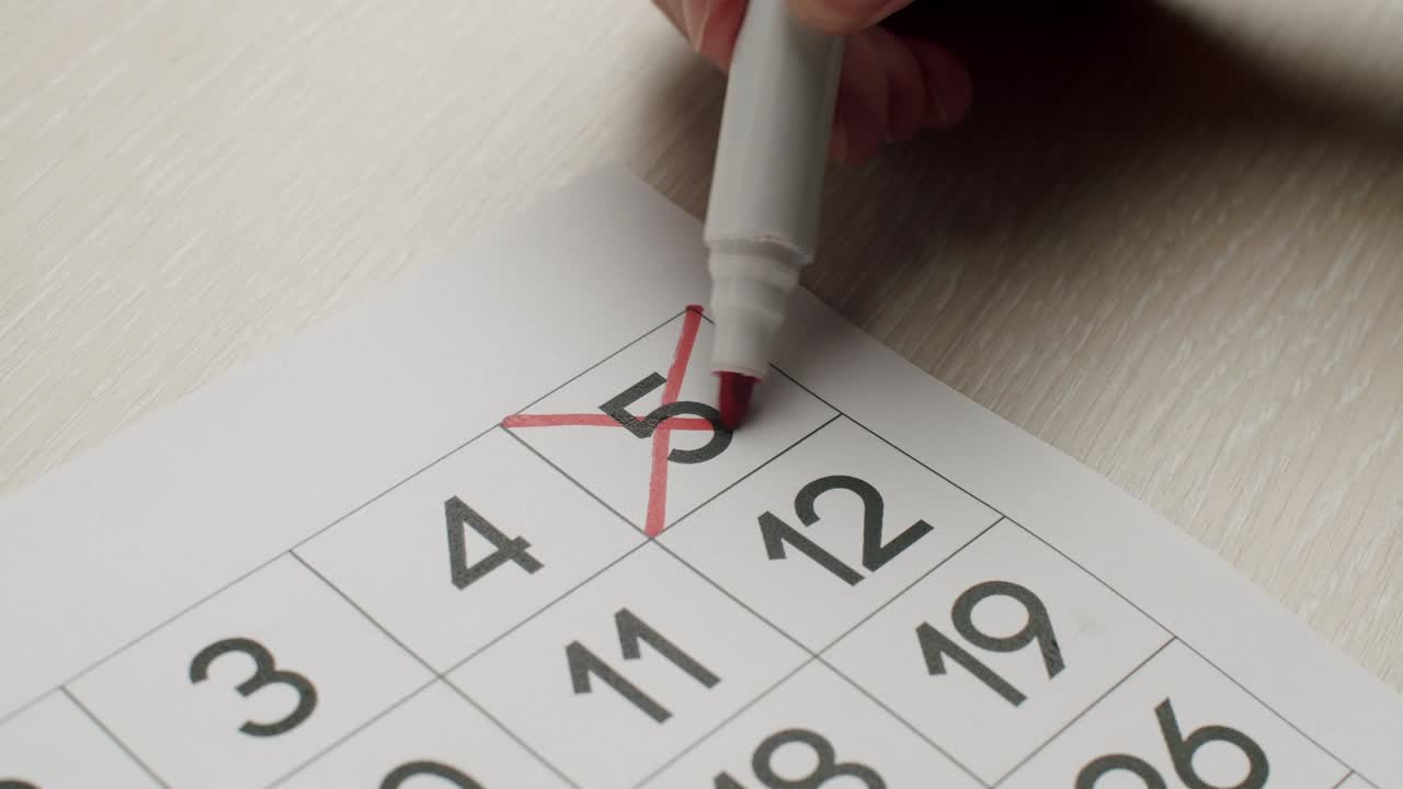 la mano del hombre escriba el quinto día en el calendario de papel usando un bolígrafo rojo.