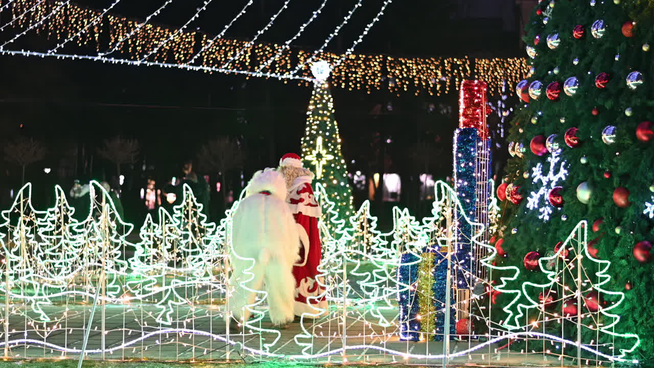 Visitors enjoy a festive park adorned with bright holiday lights. A snowman and Santa celebrate the season among decorated trees and cheerful decorations, creating a joyful atmosphere