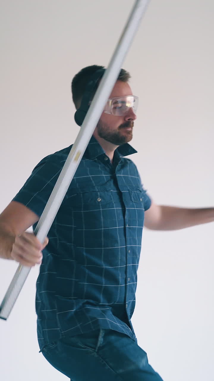 happy girl with ponytail shoots boyfriend dancing with professional level tool by white wall at construction in empty flat