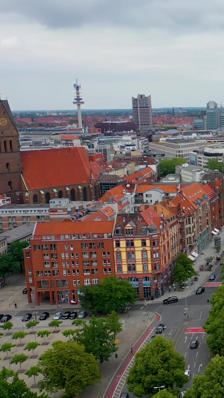 Ripresa verticale cinematografica con drone dello skyline della città di Hannover, con la storica Chiesa del Mercato, tetti rossi e traffico urbano. Prospettiva dall'alto dell'architettura tedesca e della vita cittadina.