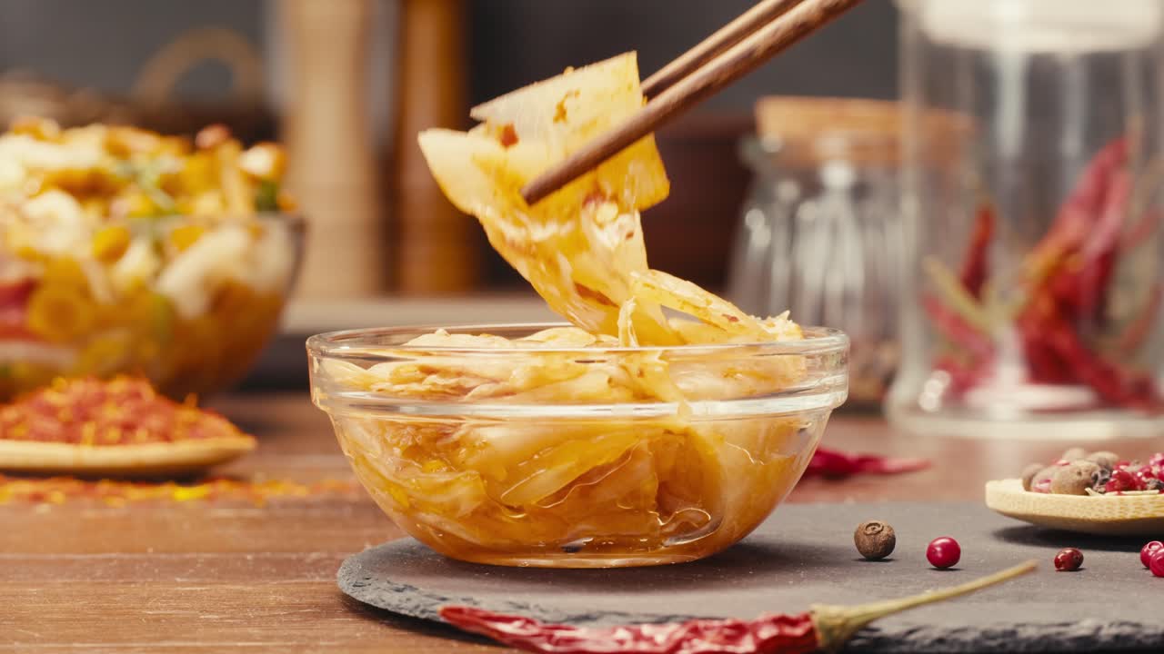Taking a little bit of fermented spicy cabbage kimchi with chopsticks close-up. Preservation of vegetables in glass jars. Fermentation preserved kimchi cabbage with spices macro. Asian cuisine.