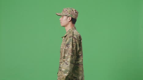 vista lateral del hombre asiático soldado caminando en la pantalla verde estudio de fondo