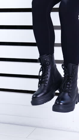 unrecognized female in black tight pants and heavy boots sitting on a window sill. model demonstrating fashionable autumn footwear. vertical video