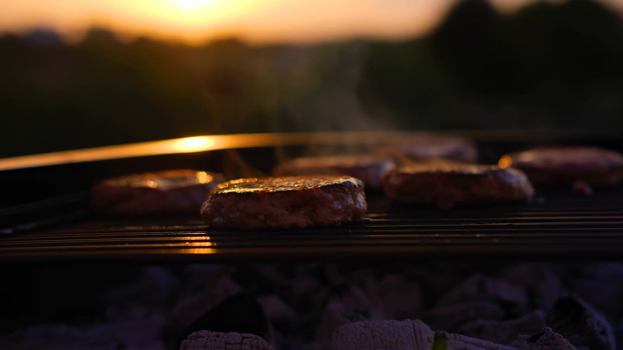 Griglia Al Tramonto Con Hamburger Sfrigolanti, Carboni Ardenti, Fumo Leggero Che Sale, Paesaggio Con Bokeh Morbido, Caldo