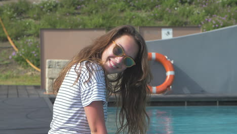 a young woman in sunglasses smiles at the camera while sitting by the pool