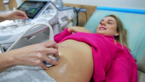 beautiful smiling lady lies having ultrasound examination. doctor's hand holds the ultrasonic device on woman's belly. close up.