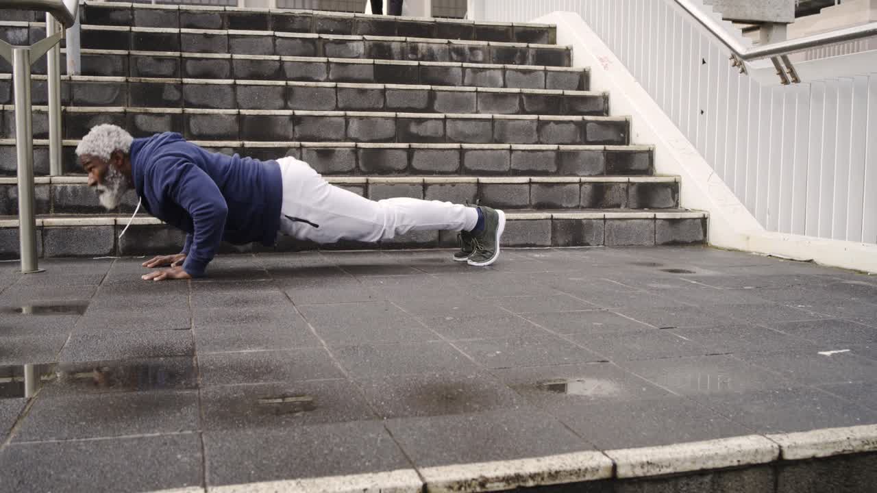 Senior African American man starting plank doing push-ups on stairs as pedestrian crossing behind
