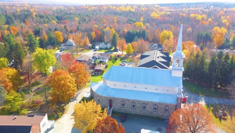 historic church surrounded by fall foliage drone view in estrie, québec, canada.