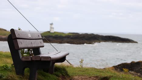 a bench facing a lighthouse across the sea