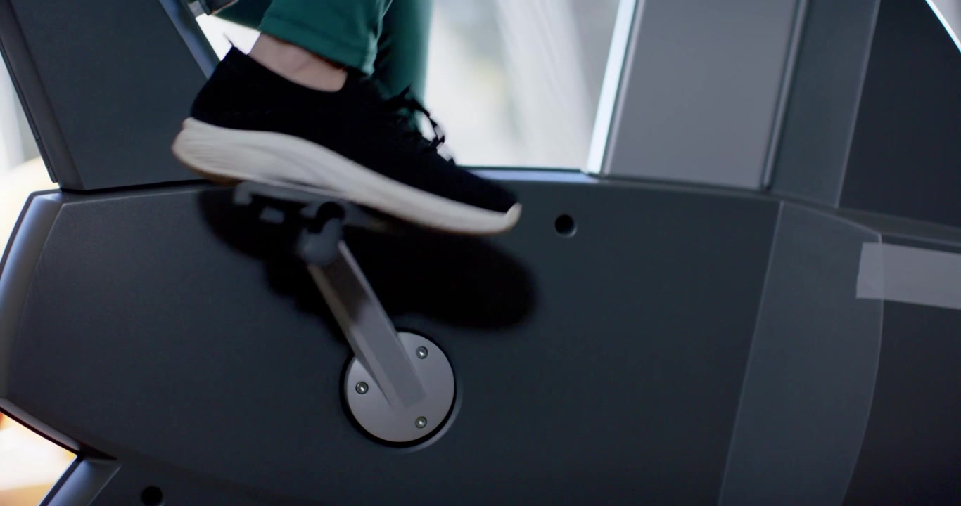 Piede destro che preme e pedala per fare esercizio, gambe con scarpe da ginnastica che pedalano su una macchina vicino alla finestra.