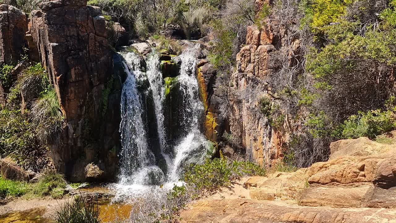 perspectiva aérea en cámara lenta de una cascada de australia occidental rodeada de rocas y arbustos australianos