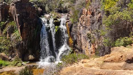 slowmotion aerial perspective of western australian waterfall surrounded by rock and australian bush