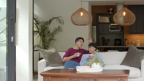 relaxing at home, multiracial gay couple sitting on sofa and drinking coffee