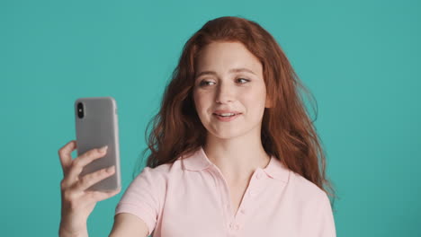 Redheaded-girl-in-front-of-camera-on-turquoise-background.