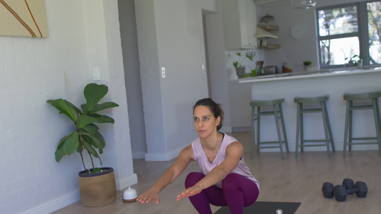 Video verticale: Donna a casa che inizia l'allenamento facendo squat lenti su un tappetino con pesi, indossando leggings.