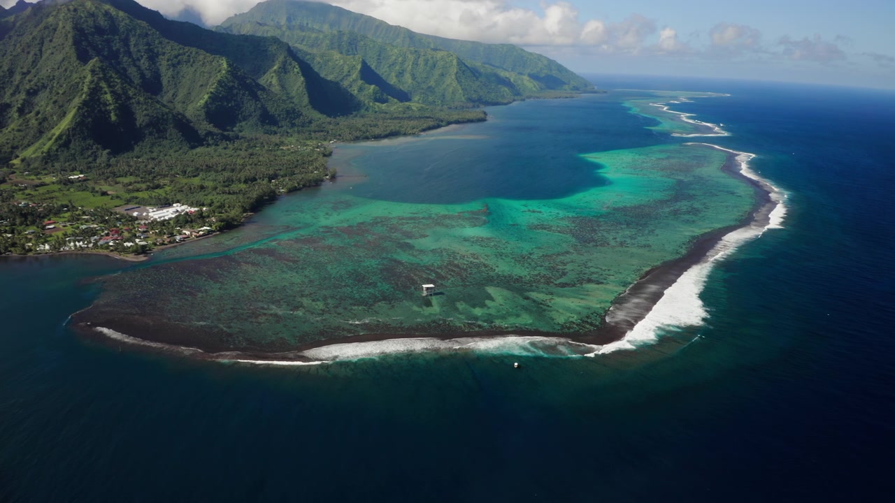 Ampia ripresa aerea con drone dalla valle di Teahupoo, Tahiti, che domina il passaggio della barriera corallina con montagne ricoperte da foresta pluviale che si ergono dietro la costa.