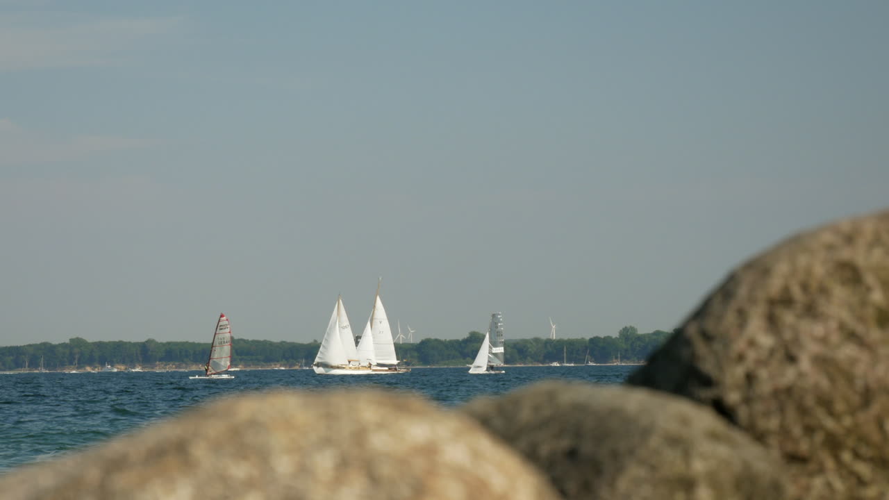 размытые скалы на переднем плане и парусники на заднем плане в ветреный день в любеке, германия