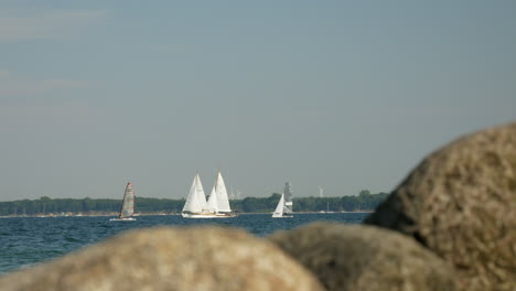 Verschwommene-Felsen-Vorn-Und-Segelboote-Im-Hintergrund-An-Einem-Windigen-Tag-In-Lübeck,-Deutschland