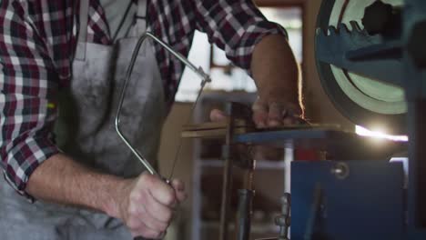 midsection of caucasian male knife maker in workshop using saw