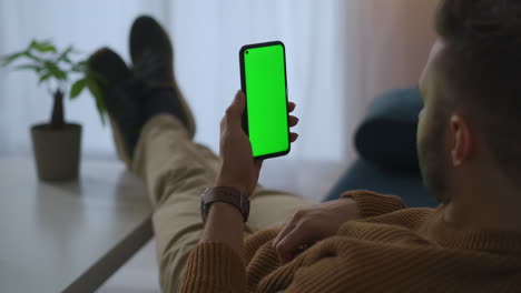 Teléfono-Inteligente-Con-Pantalla-Verde-En-Manos-De-Un-Hombre-Relajado-En-El-Hogar,-El-Usuario-Está-Navegando-Por-Sitios-De-Internet-Y-Redes-Sociales-Leyendo-Tecnología-De-Clave-Cromática-De-Libros-Electrónicos