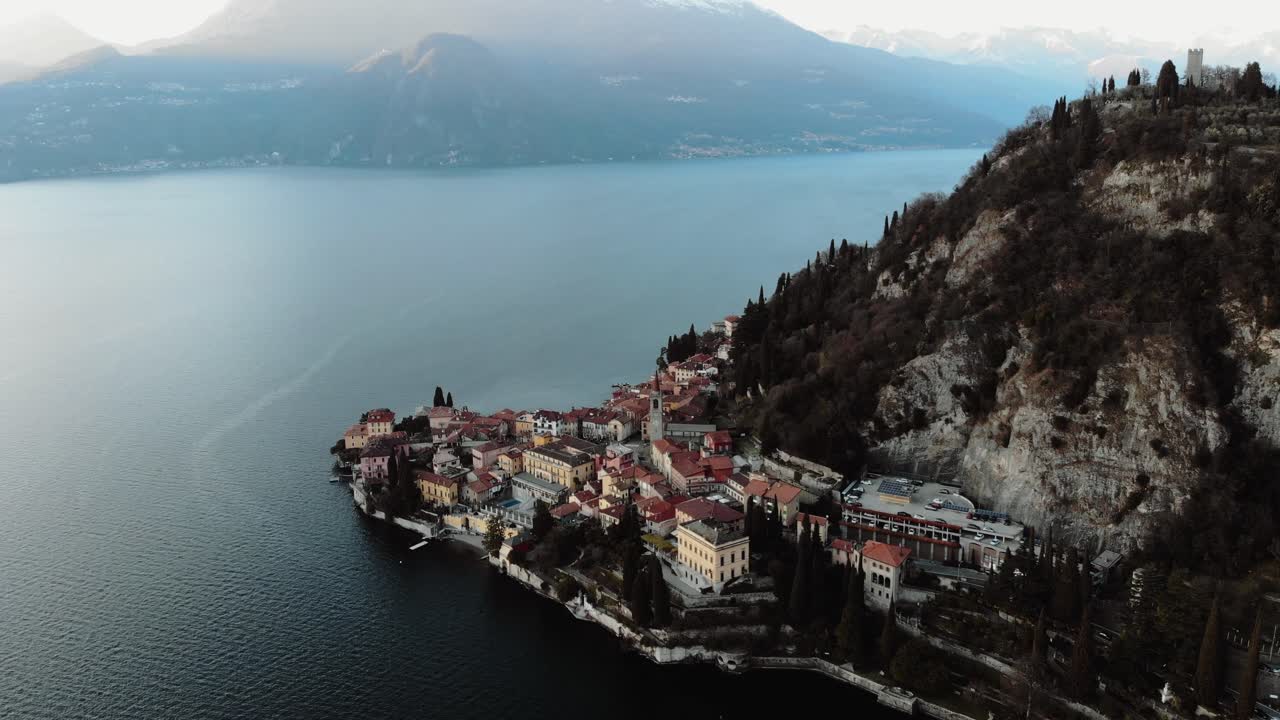 Aerial footage reveals a fog-blanketed Lake Como with silhouetted trees emerging in the serene, muted landscape. The atmosphere is tranquil, with soft, diffused lighting