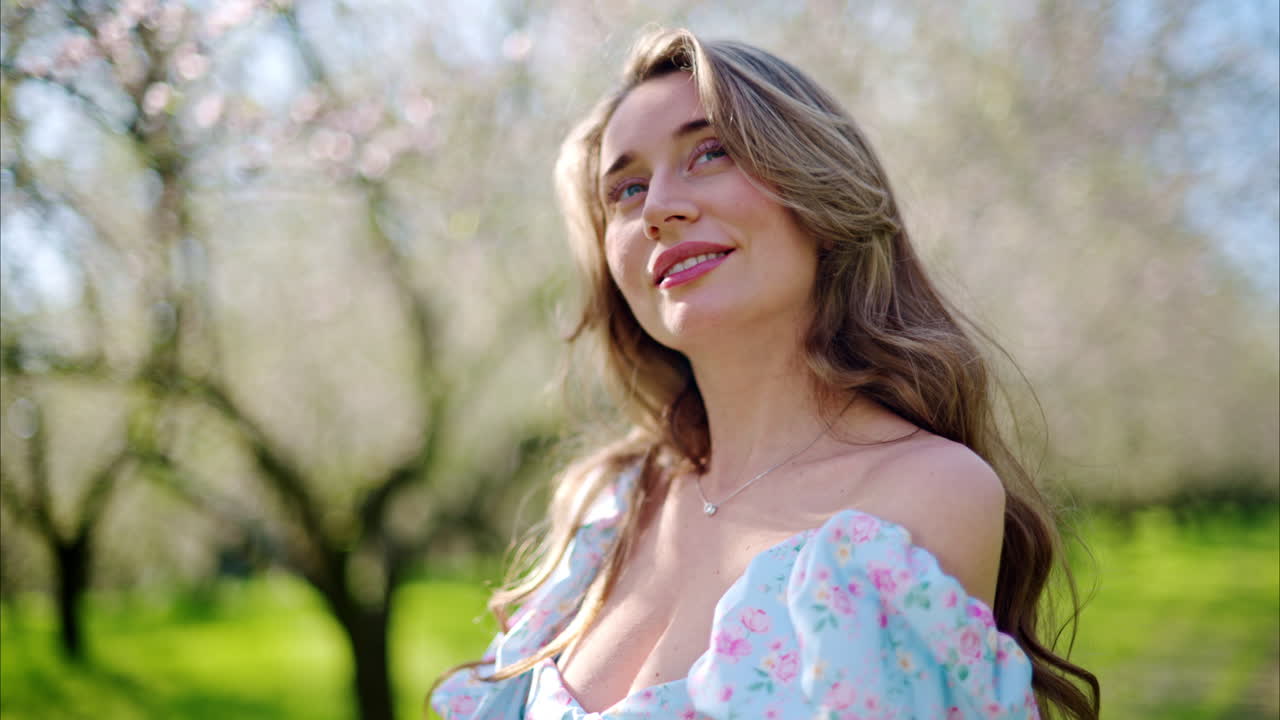 Brunette woman in a blue dress enjoying a field of blooming almond trees