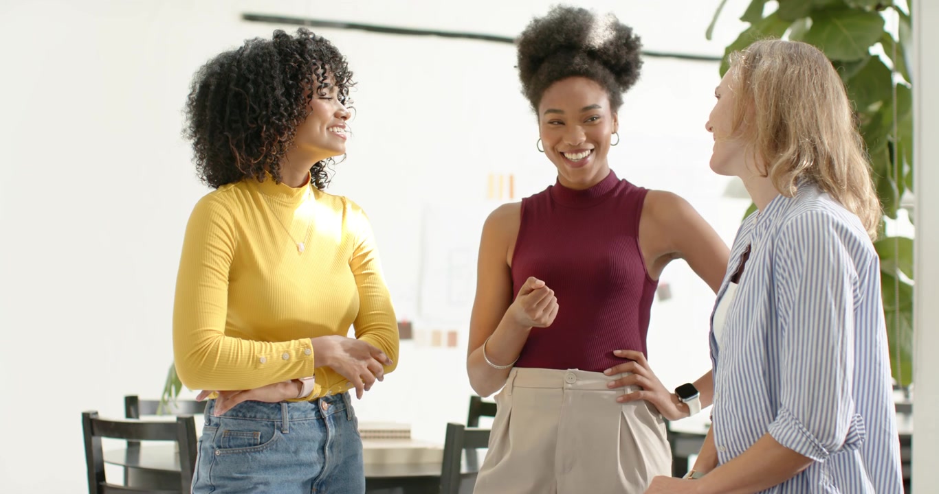 Colegas de trabalho diversas iniciando uma discussão, gesticulando para o laptop à mesa, sorrindo para o trabalho