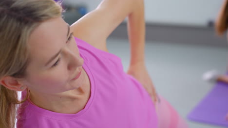 primer plano de una mujer con ropa deportiva rosa con la mano en la cintura ajustando la postura mientras mira a un amigo en el fondo, los detalles borrosos muestran a otra persona también ajustando el movimiento en la sesión de fitness