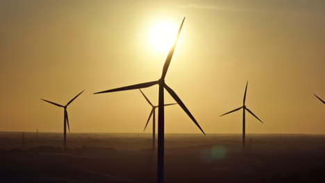 fast sideways drone shot of backlit wind turbines during a sunset