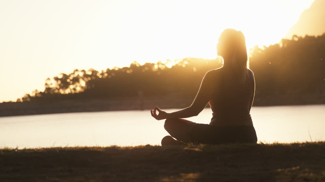 mujer meditando haciendo yoga junto a un hermoso lago y montañas al atardecer