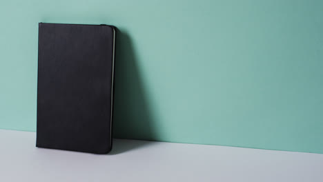 close up of closed black book leaning on wall with copy space on green background in slow motion