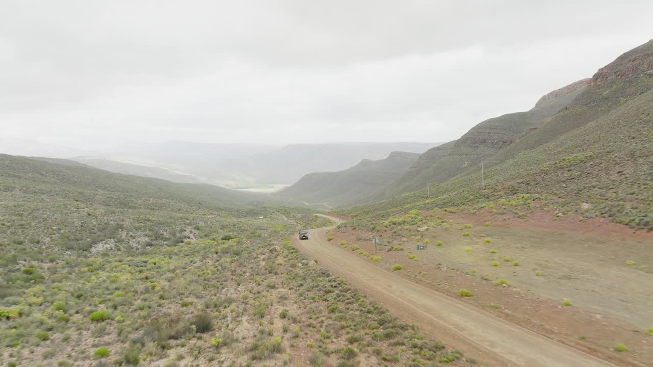 drone vuela hacia atrás sobre una carretera en el paisaje desértico donde un suv negro sube la colina en el área silvestre de cederberg en sudáfrica - en el fondo se pueden ver montañas rocosas